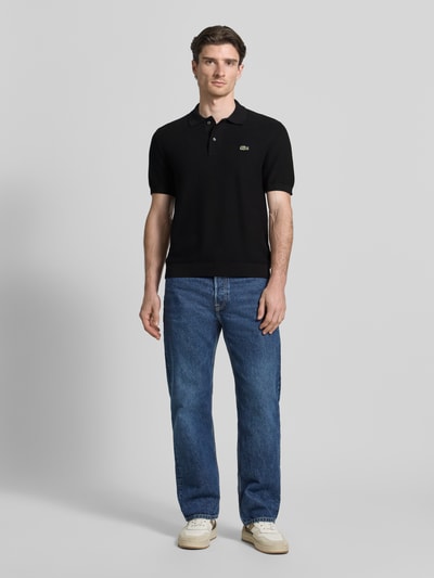 Męski model nosi Regular Fit Poloshirt aus reiner Baumwolle od Lacoste, czarny, krój regular fit, gładki, logo, krótki rękaw, prążkowane wykończenia, bawełna, widok całej sylwetki z przodu.