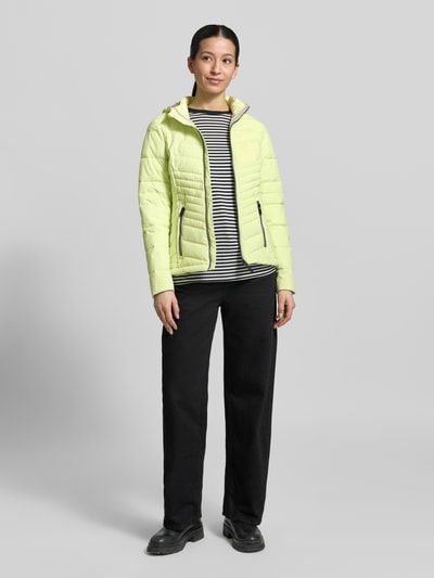 Kobiece model nosi Slim Fit Jacke in Stepp-Optik od G.I.G.A. DX w jasnożółtym kolorze z efektem pikowania, odpinany kaptur, detal z logo, zamek błyskawiczny, wpuszczane kieszenie z zamkiem, długość tyłu w rozmiarze 36: 60 cm, szerokość ramion w rozmiarze 36: 45 cm, szerokość w rozmiarze 36: 46 cm, długość rękawów w rozmiarze 36: 64 cm, pełny widok z przodu.