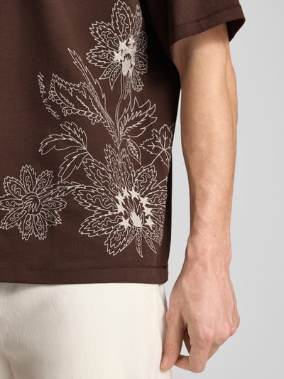 Männermodel trägt Loose Fit T-Shirt mit Stitchings von Scotch & Soda in Braun mit weißem Blumenmuster, Reine Baumwolle, Nahaufnahme Oberkörper.