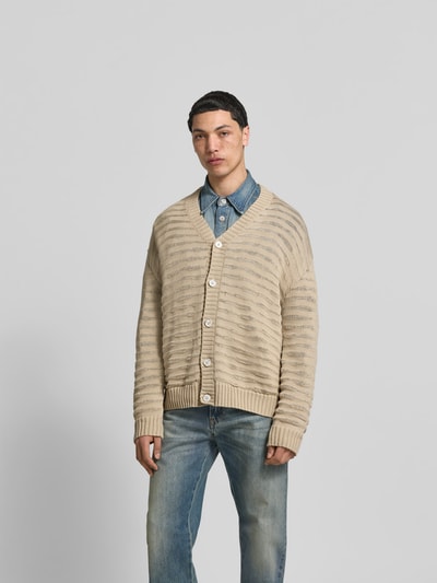 Männermodel trägt Relaxed Fit Cardigan in Strick-Optik von MM6 Maison Margiela aus reiner Baumwolle, beige mit Knopfleiste, Ganzkörperansicht von vorne.