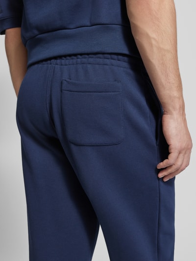 Mężczyzna nosi Loose Fit Sweatpants aus reiner Baumwolle von Lacoste w kolorze granatowym, pojedynczy kolor, elastyczny pas, tylna kieszeń, materiał bawełniany typu sweat, detal z logo, widok z tyłu, zbliżenie na dolną część pleców.