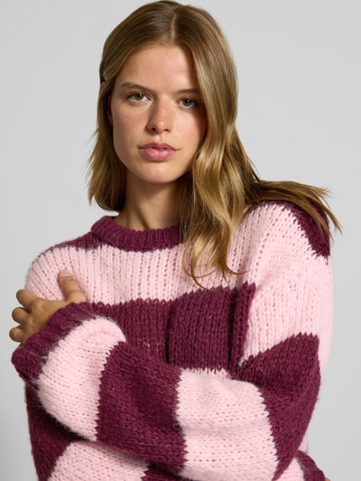 Frauenmodel trägt Relaxed Fit Pullover im Chunky Knit Look Modell 'DORTHEA' von PIECES in Rosa und Bordeaux, grob gestrickte Textur, Nahaufnahme Oberkörper. Damen Pullover von PIECES