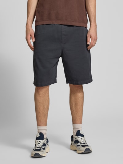 Männermodel trägt Shorts mit Gesäßtasche Modell 'Floyde' von Carhartt Work In Progress im Lyocell-Mix, Loose-Fit, dunkles Uni, Ganzkörperansicht von vorne. Im Kontext: Herren Shorts, Lyocell-Mix mit Baumwoll-Anteil, Elastischer Bund mit Kordelzug, Seitliche Eingrifftaschen, Bundweite bei Größe M: 37 cm, Innenbeinlänge bei Größe M: 24 cm.