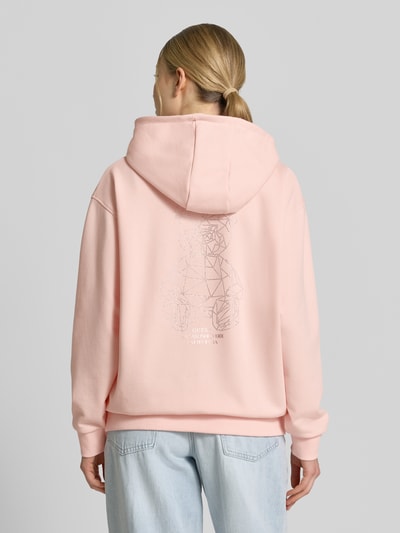 Vrouwenmodel draagt Oversized Hoodie met strasssteendecoratie model 'Silvy' van Guess Activewear, katoenmix, oversized fit, capuchon, kangoeroezak, elastische boorden, lichtroze tint, zachte textuur, volledige achterkant weergave.