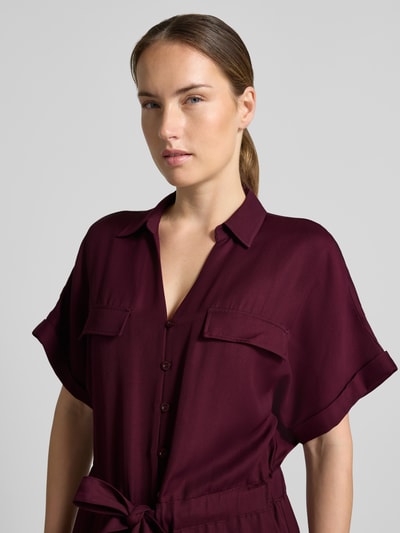 Frauenmodel trägt Jumpsuit aus Viskose-Lyocell-Mix von MORE & MORE in Dunkelrot mit Umlegekragen, Taillenband, Nahaufnahme Oberkörper.
