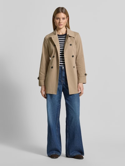 Vrouwenmodel draagt Regular fit trenchcoat met tailleriempje om te strikken model 'CHALSEA OLIVIA' van Vero Moda, effen ontwerp, twill structuur, dubbele knoopsluiting, steekzakken, lange mouw met riempje, voorkant volledige lichaamsopname.