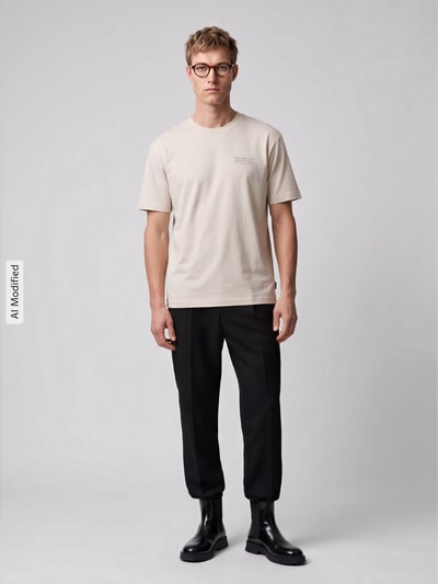 Männermodel trägt Boxy Fit Shirt aus Baumwoll-Mix von Marc O'Polo DENIM in Beige mit glatter Textur, schwarze Hose, Ganzkörperansicht von vorne, KI-modifiziertes Bild.