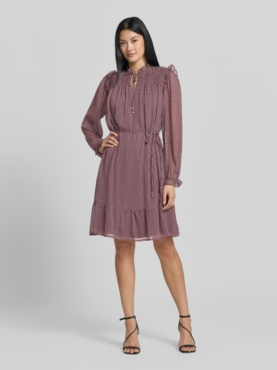 Frauenmodel trägt Knielanges Kleid mit Bindegürtel von Christian Berg Woman Selection, A-Linie, Allover-Look, Smok-Details, Rüschen, transparent wirkende lange Ärmel, in zarten Rottönen mit feinem Muster, fließende Textur, Bindegürtel, Ganzkörperansicht von vorne.