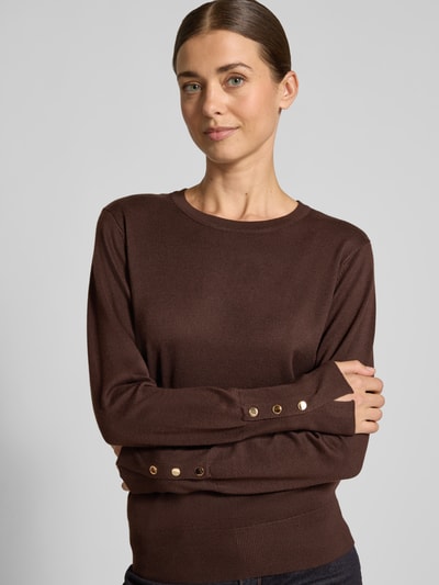 Modelka nosi brązowy Strickpullover aus Viskose-Mix Modell 'KATIE' von FREE/QUENT, krój regular fit, okrągły dekolt, guziki na rękawie, tekstura gładka, kontekst: damski sweter z domieszką stretchu, długość tyłu 51 cm, długość rękawa 63 cm, zbliżenie górnej części ciała.