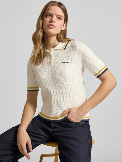Frauenmodel trägt Regular Fit Poloshirt mit Zopfmuster und Logo-Stitching von Karo Kauer aus Viskose-Mix mit Polokragen und kurzer Knopfleiste, creme mit farbigen Bündchen, Rückenlänge bei Größe S 52 cm, Ärmellänge 23 cm, Nahaufnahme Oberkörper.