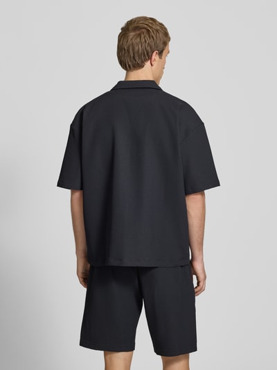 Männermodel trägt schwarzes Relaxed-Fit Freizeithemd mit Reverskragen Modell 'Troy' von Pegador, Strukturmuster, Ganzkörperansicht Rückansicht. Rückenlänge bei Größe M 67 cm, Schulterbreite 49 cm, Ärmellänge 24 cm, Kurzärmelig, durchgängige Knopfleiste, Logo-Stitching.