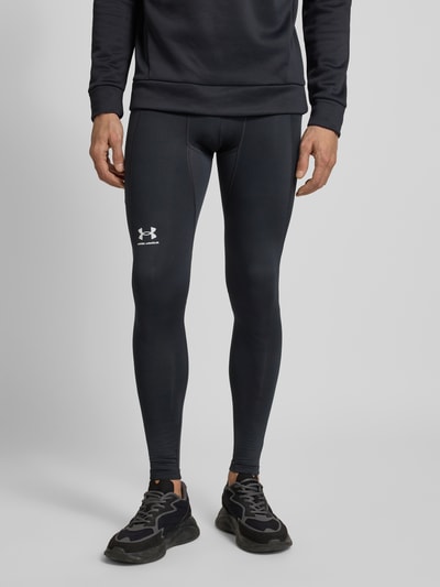 Męski model nosi Leggings mit elastischem Bund und Logo von Under Armour, ciemny materiał z domieszką stretch, logo, widok całej sylwetki z przodu.
