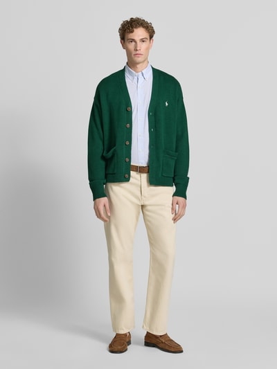 Männermodel trägt Relaxed Fit Strickjacke aus reiner Baumwolle von Polo Ralph Lauren in Dunkelgrün, kombiniert mit heller Hose, Herren, Ganzkörperansicht von vorne.