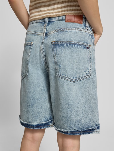 Männermodel trägt Relaxed Fit Jeansshorts aus Baumwoll-Lyocell-Mix von Tommy Jeans, stylizowana na denim, efekt znoszenia, naszywka z logo, mieszanka bawełny i lyocellu, 5 kieszeni, wykończenie frędzlami, szlufki na pasek, zapięcie na guzik i zamek błyskawiczny, widok całej sylwetki od tyłu.