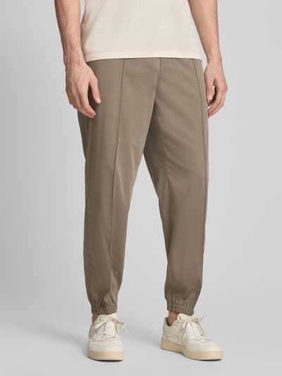 Männermodel trägt Regular Fit Stoffhose aus Viskose-Mix mit elastischem Bund von ARMANI EXCHANGE in Beige mit Ziernähte, Ganzkörperansicht von vorne. Bundweite Größe 32: 44 cm, Innenbeinlänge: 77 cm, elastische Beinabschlüsse, Gesäßtaschen.