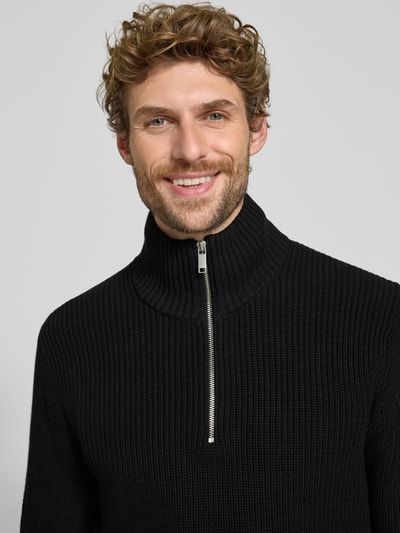 Männermodel trägt Slim Fit Strickpullover aus reiner Baumwolle mit Troyer-Kragen von MCNEAL, schwarze Farbe, Nahaufnahme Oberkörper.