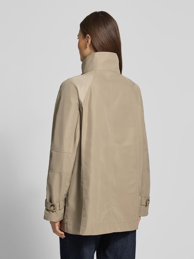 Modelka kobieca ma na sobie beżowy Trenchcoat mit Stehkragen und Ärmelriegeln od Fuchs Schmitt, krój relaxed fit, gładka tekstura, długie rękawy z paskami, długość tyłu w rozmiarze 36: 72 cm, szerokość ramion w rozmiarze 36: 40 cm, szerokość w biuście w rozmiarze 36: 54 cm, długość rękawa w rozmiarze 36: 60 cm, widok całej sylwetki z tyłu.