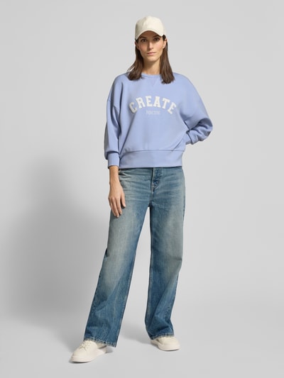 Kobiece model prezentuje Sweatshirt aus Viskose-Mix mit Rundhalsausschnitt Modell 'CELLI' od MOS MOSH w kolorze jasnoniebieskim, z nadrukiem CREATE, relaxed fit, damska bluza z domieszką stretchu, jeansy, białe sneakersy i czapka, zdjęcie: całopostaciowe z przodu.