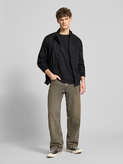 Męski model nosi Regular Fit Kurtka z stójką Model 'Hefi' od Blend, czarna, bawełna, zamek błyskawiczny, wpuszczane kieszenie, elastyczne wykończenia, długość tyłu w rozmiarze M 71 cm, szerokość ramion 46 cm, szerokość w rozmiarze M 48 cm, długość rękawów 25 cm, całkowity widok z przodu.