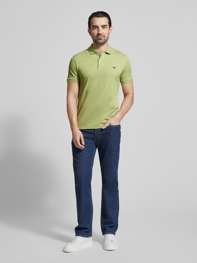 Männermodel trägt Slim Fit Poloshirt aus reiner Baumwolle von Lacoste, Optik: Unifarben, Logo-Stitching, Polokragen, Ganzkörperansicht von vorne.