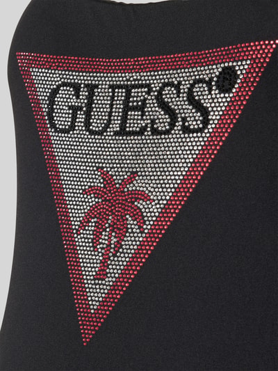 Frauenmodel trägt Slim Fit Badeanzug mit Strasssteinbesatz von Guess aus elastischem Material-Mix, mit Logo-Detail, Nahaufnahme Oberkörper.
