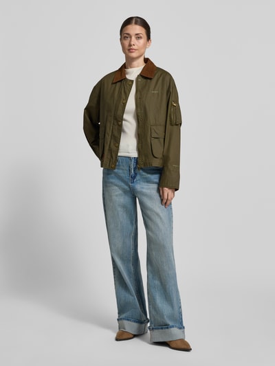 Frauenmodel trägt Jacke aus Baumwolle mit Pattentaschen von Original Bombers in Olivgrün, Regular-Fit, Umlegekragen, Knopfleiste, Ganzkörperansicht von vorne. Rückenlänge 60 cm, Schulterbreite 52 cm, Brustweite 58 cm, Ärmellänge 57 cm, Reine Baumwolle.