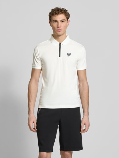 Männermodel trägt Slim Fit Poloshirt aus Viskose-Mix von EA7 Emporio Armani in Weiß mit Logo-Detail, Polokragen, elastische Ärmelabschlüsse; Ganzkörperansicht von vorne.