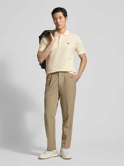 Männermodel trägt Regular Fit Poloshirt aus reiner Baumwolle von Lacoste in Beige, uni, Piqué-Textur, Logo-Stitching, Ganzkörperansicht von vorne.