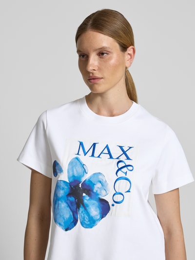 Frauenmodel trägt weißes Boxy-Fit Damen T-Shirt aus reiner Baumwolle Modell 'MAMBO' von MAX&Co. mit blauem Print, Nahaufnahme Oberkörper.