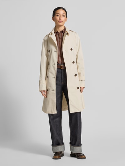 Modelka nosi Regular Fit Trenchcoat aus Baumwoll-Mix od s.Oliver RED LABEL, beżowy, z kołnierzem, długie rękawy, bawełniany splot, kieszenie z patkami, szlufki na pasek, dwurzędowe guziki, prosty fason, widok całej sylwetki z przodu.