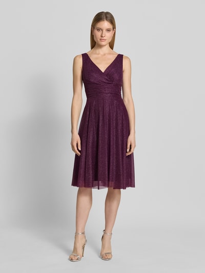 Frauenmodel trägt Knielanges Cocktailkleid mit V-Ausschnitt von TROYDEN COLLECTION aus Chiffon in Dunkellila, Taillierter Schnitt, Breite Träger, Rückseitiger V-Ausschnitt, Rückenreißverschluss, Rückenlänge bei Größe 36: 85 cm, Brustweite bei Größe 36: 43 cm, Ganzkörperansicht von vorne.