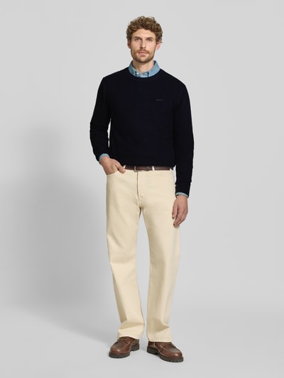Männermodel trägt Regular Fit Pullover aus Baumwoll-Woll-Mix von GANT in Dunkelblau, kombiniert mit heller Hose, Ganzkörperansicht von vorne.