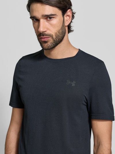 Mężczyzna-model nosi Slim Fit T-Shirt mit Logo-Print Modell 'Vanish' von Under Armour w kolorze ciemnoszarym, z okrągłym dekoltem, ażurowa faktura, szerokość w rozmiarze M: 40 cm, długość nogawki wewnętrznej 70 cm, krój slim fit, zbliżenie na górną część ciała