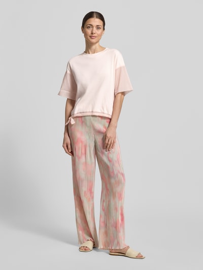 Frauenmodel trägt T-Shirt mit Rundhalsausschnitt und Tunnelzug von Marc Cain aus Baumwoll-Elasthan-Mix, Relaxed-Fit, Ärmel mit Aufschlag, Rückenlänge 51 cm bei Größe 36, zartes Rosa, glatte Textur, Ganzkörperansicht von vorne.