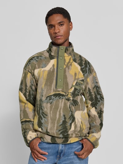 Męski model ma na sobie Fleecepullover mit Label-Patch Modell 'HELVETIA' od Columbia, prosty krój, stójka, naszywka z logo, brystasza z zamkiem, tył 73 cm, rękawy 60 cm, wielokolorowy wzór, tekstura polaru, Ganzkörperansicht von vorne.