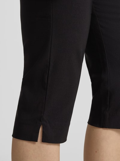 Kobieta ma na sobie Carprihose aus Viskose-Mix mit seitlichen Schlitzen von Jake*s Casual, czarny, gładki materiał, krój slim fit, elastyczny, z bocznymi rozcięciami, szerokość w rozmiarze 36: 36 cm, długość wewnętrzna nogawki w rozmiarze 36: 44 cm, zapięcie na haczyk i zamek, detaliczny widok nogawki