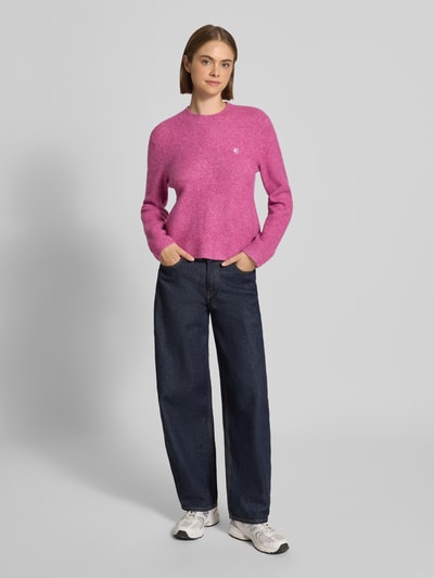Vrouwenmodel draagt gebreide pullover met labeldetail Model 'Curtis' van Carhartt Work In Progress, materiaalmix met wol, getailleerde pasvorm, ronde hals, ribboorden, kleur roze, gladde textuur, ruglengte maat S 55 cm, mouwlengte 60 cm, geheel vooraanzicht.