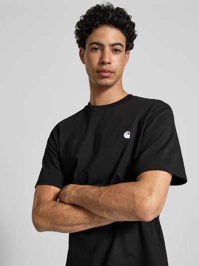 Männermodel trägt schwarzes Herren T-Shirt mit Label-Stitching Modell 'Madison' von Carhartt Work In Progress aus Reine Baumwolle, Regular-Fit, Rundhalsausschnitt, Rückenlänge bei Größe M 75 cm, Nahaufnahme Oberkörper.