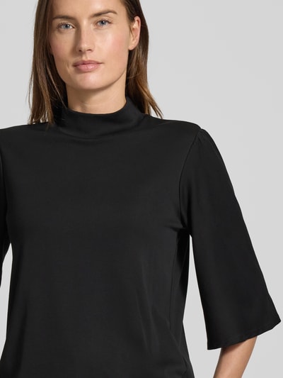 Frauenmodel trägt Longsleeve mit 3/4-Ärmel von Marc Cain aus Baumwoll-Elasthan-Mix, in Schwarz, Stehkragen, lockerer Schnitt, Nahaufnahme Oberkörper.