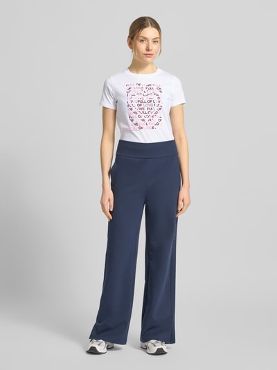 Frauenmodel trägt Regular Fit T-Shirt aus reiner Baumwolle von Tom Tailor Denim mit mehrfarbiger Optik, gestreiftem Muster, Label-Stitching-Applikation, Rundhals-Ausschnitt, Kurzarm und Jersey-Materialverarbeitung, Ganzkörperansicht von vorne.