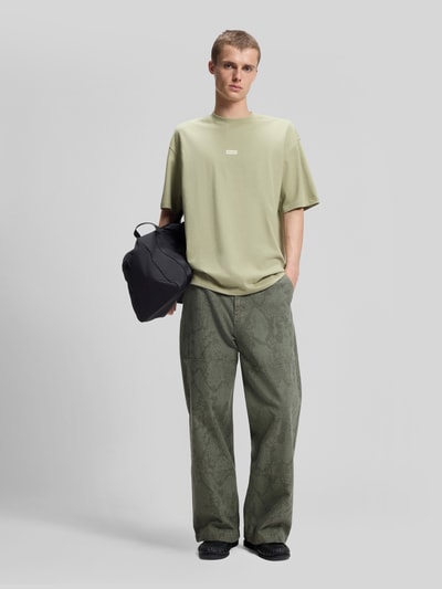 Männermodel trägt Relaxed Fit T-Shirts aus reiner Baumwolle von HUGO Blue in hellem Grün, kombiniert mit gemusterten Hosen, Ganzkörperansicht von vorne.