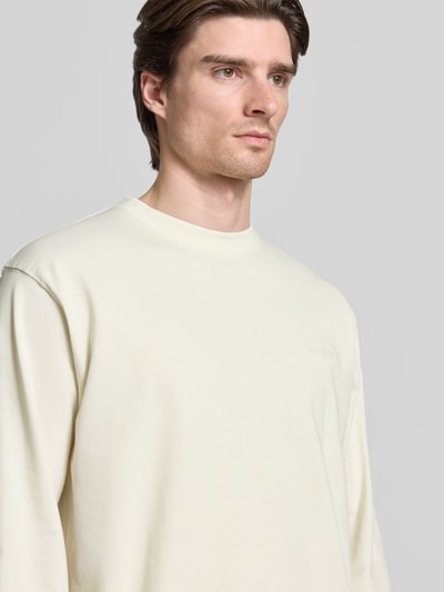 Männermodel trägt Longsleeve mit Label-Stitching Modell 'Baine' von WOODBIRD aus Bio-Baumwolle, elfenbeinfarben, Nahaufnahme Oberkörper.
