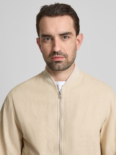 Męski model nosi Jacke aus Baumwoll-Leinen-Mix mit Zweiwege-Reißverschluss od Jack & Jones Premium w kolorze beżowym, gładka tekstura, krój regular fit, stójka, zamek błyskawiczny dwustronny, Szerokość w rozmiarze M: 54 cm, szerokość ramion w rozmiarze M: 45 cm, długość rękawów w rozmiarze M: 66 cm, długość tyłu w rozmiarze M: 68 cm, mieszanka bawełny i lnu, nahaufnahme górnej części ciała