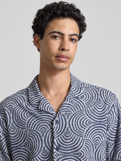 Męski model nosi Relaxed Fit Freizeithemd mit Baumwoll-Anteil Modell 'CLEMENT' od Only & Sons, wzór allover, tkanina frotte, krótki rękaw, resortkragen, mix bawełny, półzbliżenie na górną część ciała.