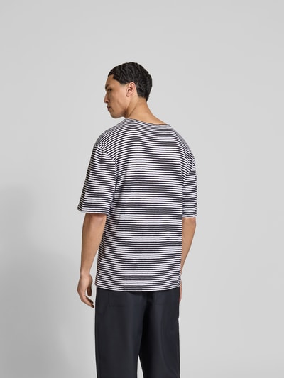Männermodel trägt Regular Fit T-Shirt aus Leinen-Mix von Officine Générale, schwarz-weiß gestreift, Halbarm, Rückenlänge 75 cm, Ganzkörperansicht Rückansicht.