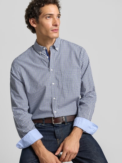 Męski model nosi Regular Fit Freizeithemd mit Button-Down-Kragen von Christian Berg Men z bawełny, kratka vichy, listwa guzikowa, kołnierzyk typu button down, długość tyłu w rozmiarze M: 80 cm, szerokość w rozmiarze M: 50 cm, długość rękawów w rozmiarze M: 66 cm, tekstura miękka, kolory granat, biel, widoczna cała sylwetka, ujęcie z przodu, zbliżenie na górną część ciała.