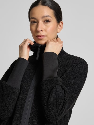 Frauenmodel trägt schwarze Fleecejacke mit Stehkragen Modell 'TOLA' von Didriksons, strukturierte Oberfläche, Nahaufnahme Oberkörper, Relaxed-Fit, Reißverschluss, Rückenlänge 83 cm, Schulterbreite 52 cm, Brustweite 47 cm, Ärmellänge 56 cm, Größe 36.