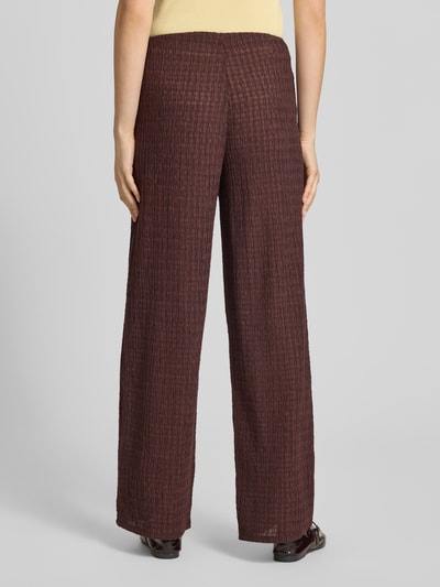 Frauenmodel trägt Straight Leg Hose in Strukturoptik Modell 'ILSE' von Only, Optik: Unifarben, Passform: Straight Leg, Bundhöhe: Mid Waist, Bundabschluss: elastisch, Materialverarbeitung: Crinkle, dunkelbraune Farbe, Stoff mit Crinkle-Textur, Ganzkörperansicht Rückansicht.