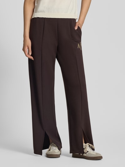 Vrouwenmodel draagt Straight Fit Sweatpants uit elastische viscosemix van Armani Exchange, donkerbruin met labeldetail, pijpsplits, elastische band, binnenbeenlengte maat S 77 cm, detailopname onderlichaam van voren.