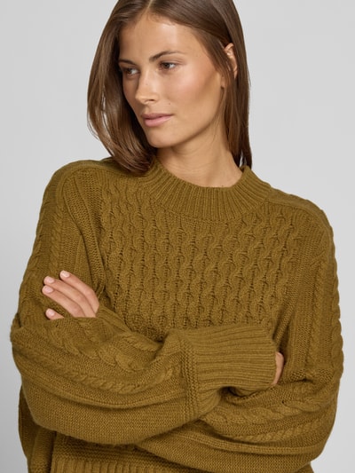 Frauenmodel trägt Strickpullover mit Zopfmuster von Style Icon Collection in Olivgrün, reine Baumwolle, lockere Passform, Nahaufnahme Oberkörper.